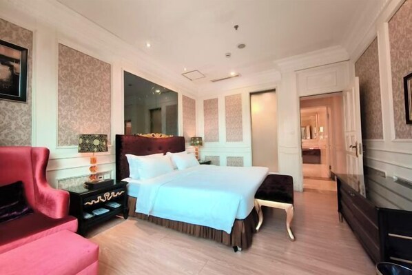 A spacious bedroom with a large bed, a red armchair, a nightstand, and a dresser. - Huaxia Conifer Hotel (Dazhou)