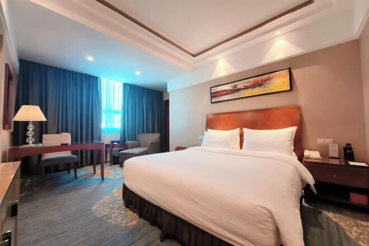A hotel room with a large bed, a desk, a chair, and a desk lamp.