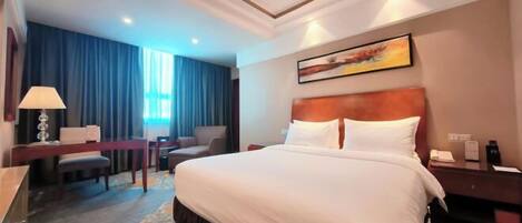 A hotel room with a large bed, a desk, a chair, and a desk lamp.