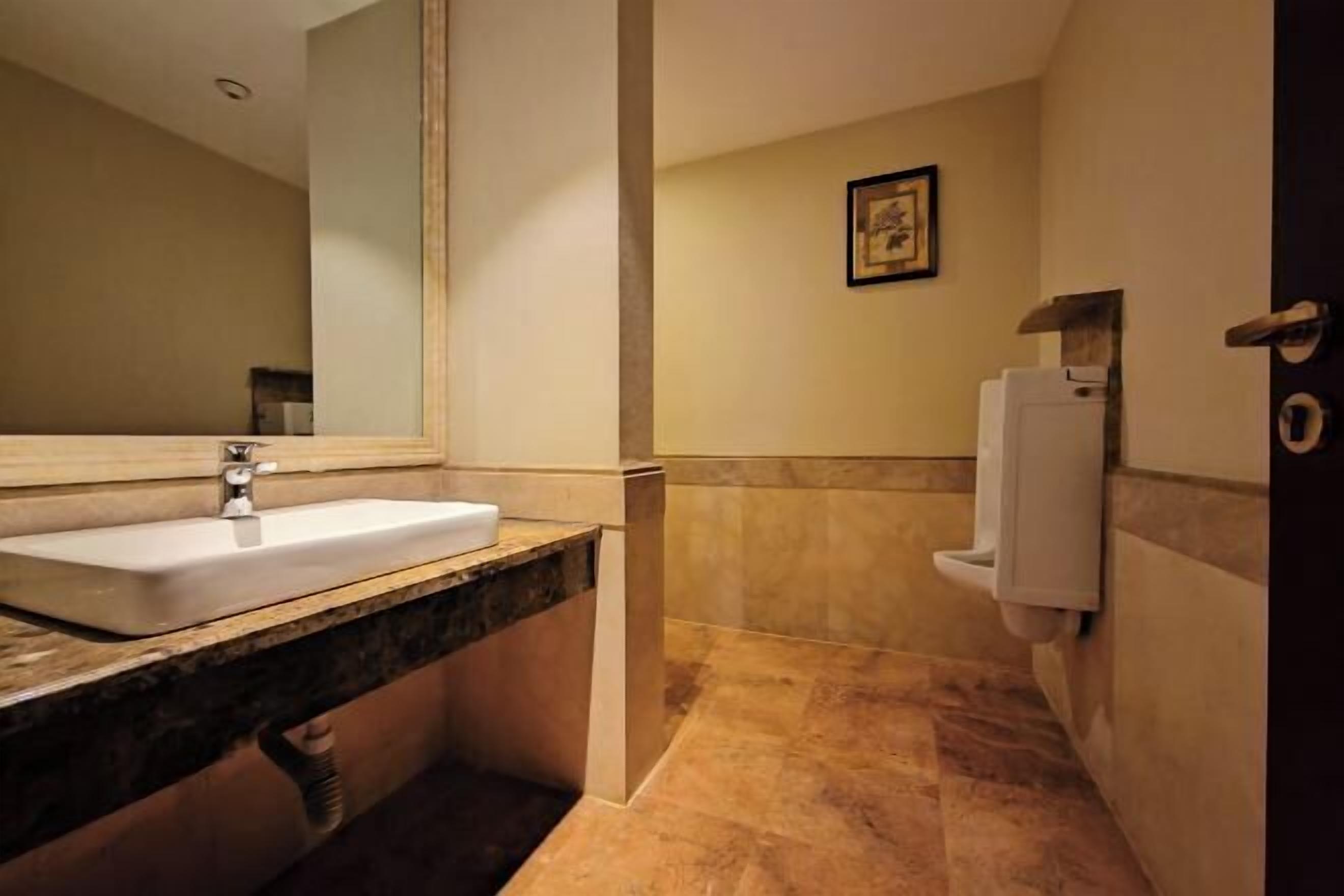 A bathroom with a sink, mirror, toilet, and a framed picture on the wall.