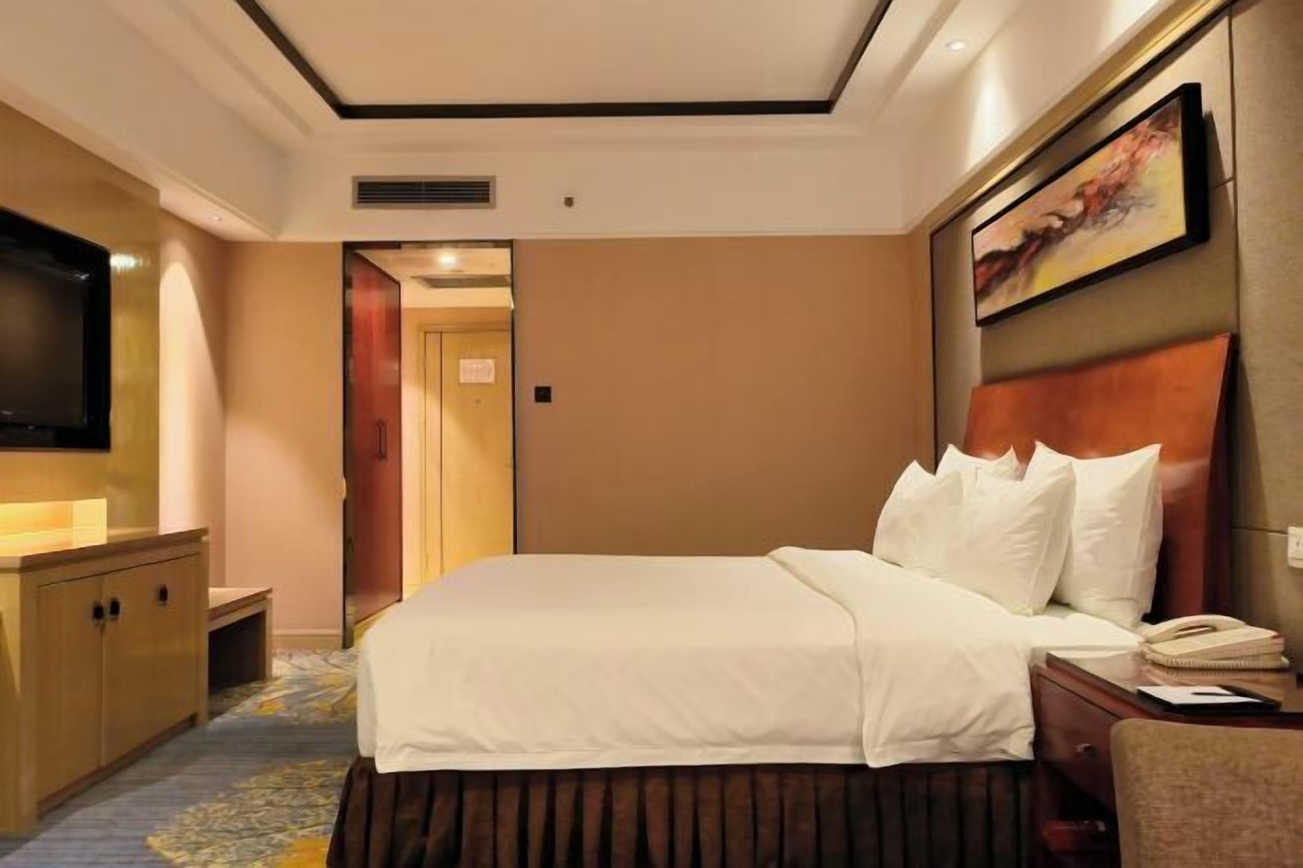 A hotel room with a bed, a TV, a desk, and a painting on the wall.
