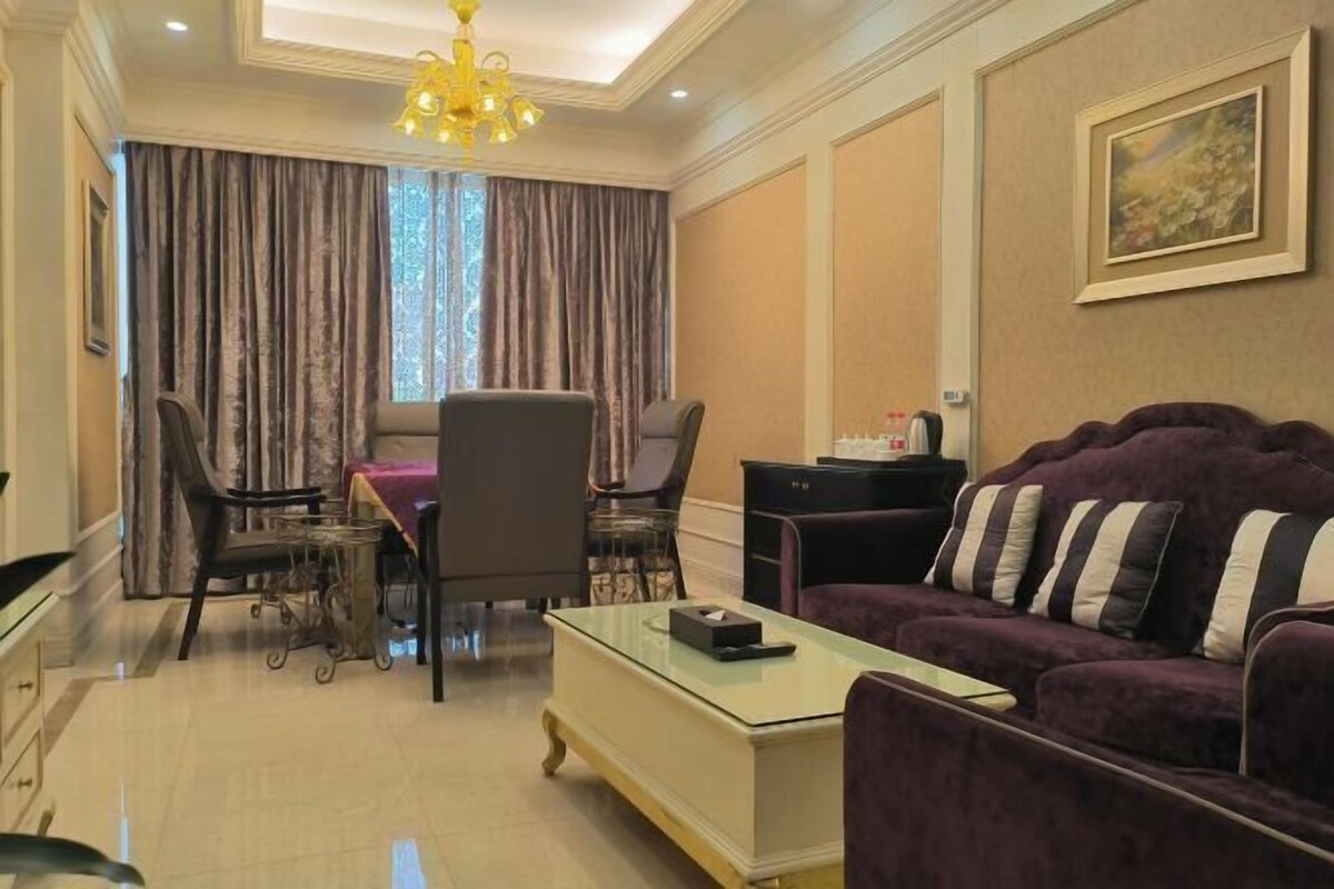 A living room with a purple sofa, a glass coffee table, a dining area with a table and chairs, and a chandelier.