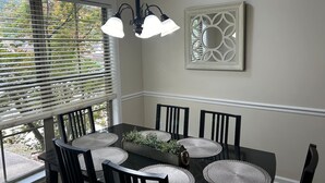 Un coin repas avec une table noire, six chaises et un lustre.