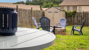 Un jardin avec une table ronde, deux fauteuils Adirondack, une clôture en bois et un abri de jardin.