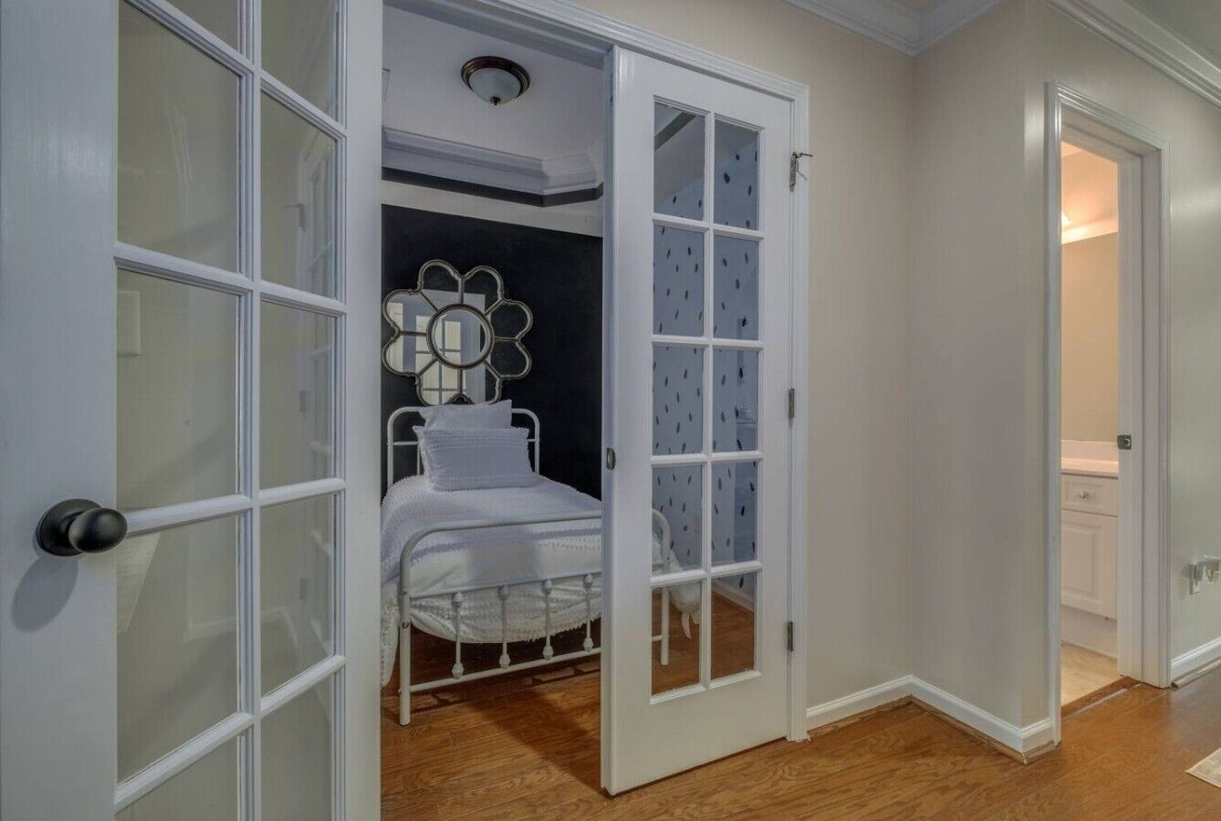 Une pièce avec un lit, une porte blanche dotée de panneaux de verre et un luminaire au plafond.