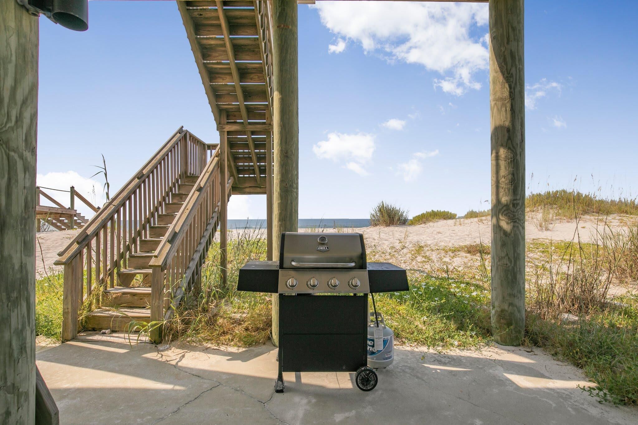 A wooden staircase leading to a beach area with a portable grill.