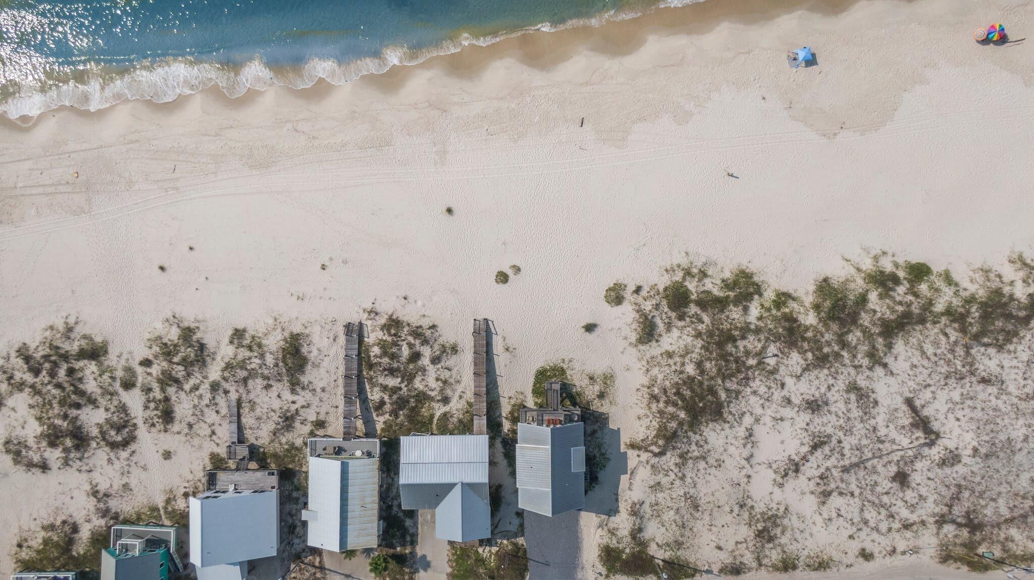 Luftaufnahme eines Strandes mit einer Reihe von Industriegebäuden und einer sandigen Küstenlinie.