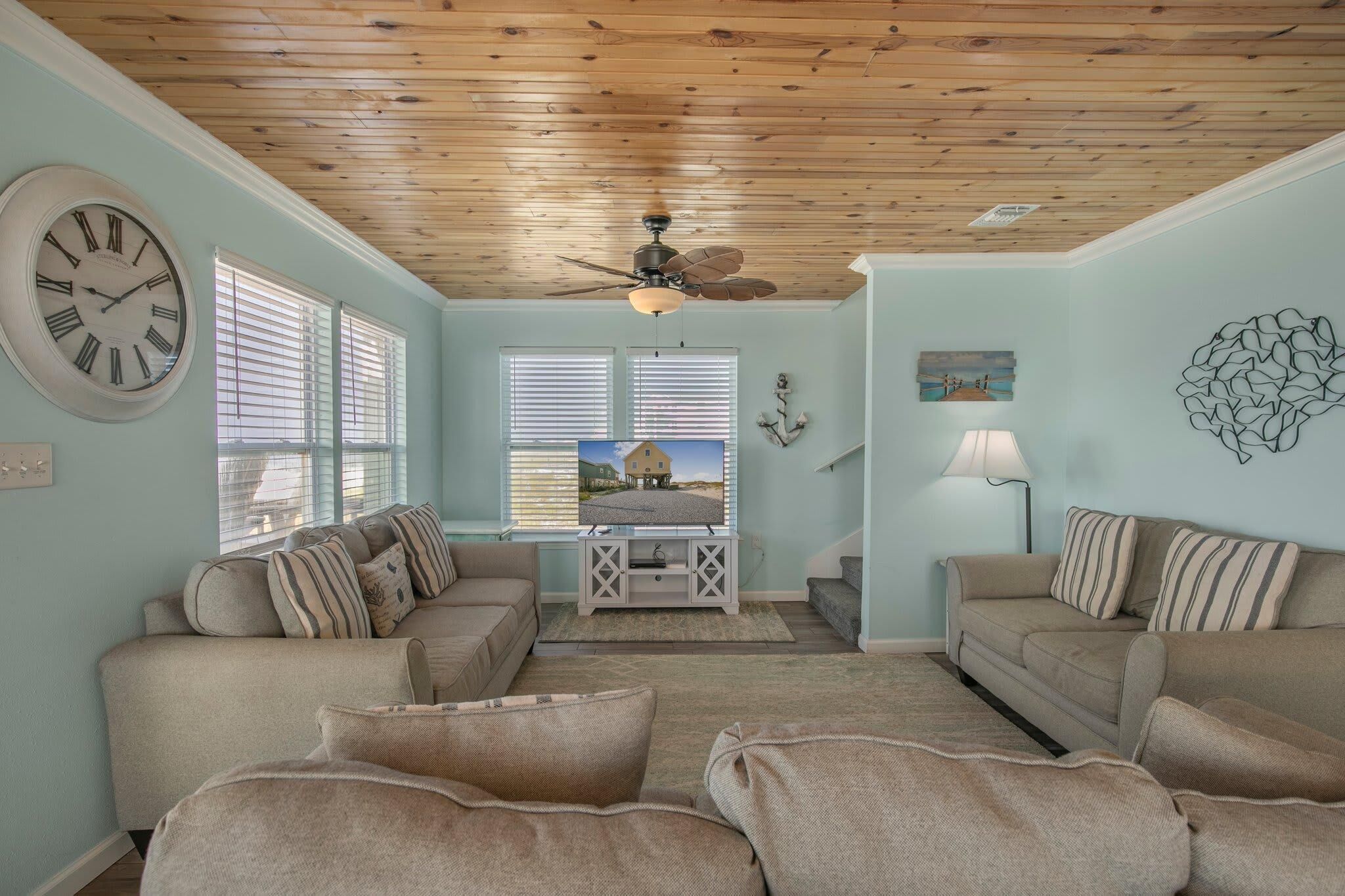 A living room with two sofas, a ceiling fan, and a large clock on the wall.