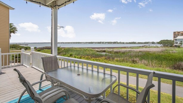 A covered outdoor area with a table and chairs, overlooking a body of water and a distant shoreline. - Blue Laguna (Gulf Shores)