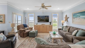 A spacious living room with a large window, a ceiling fan, and a view of the ocean. - Blue Laguna (Gulf Shores)