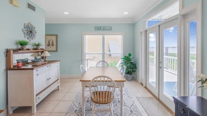 A dining area with a table and chairs, a kitchen counter, and a view through a glass door to an outdoor deck. - Blue Laguna (Gulf Shores)