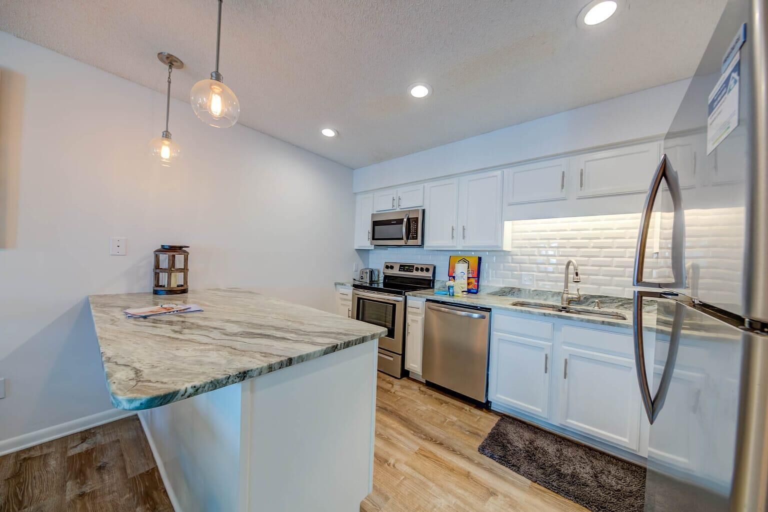 A modern kitchen with white cabinets, stainless steel appliances, and a marble countertop.