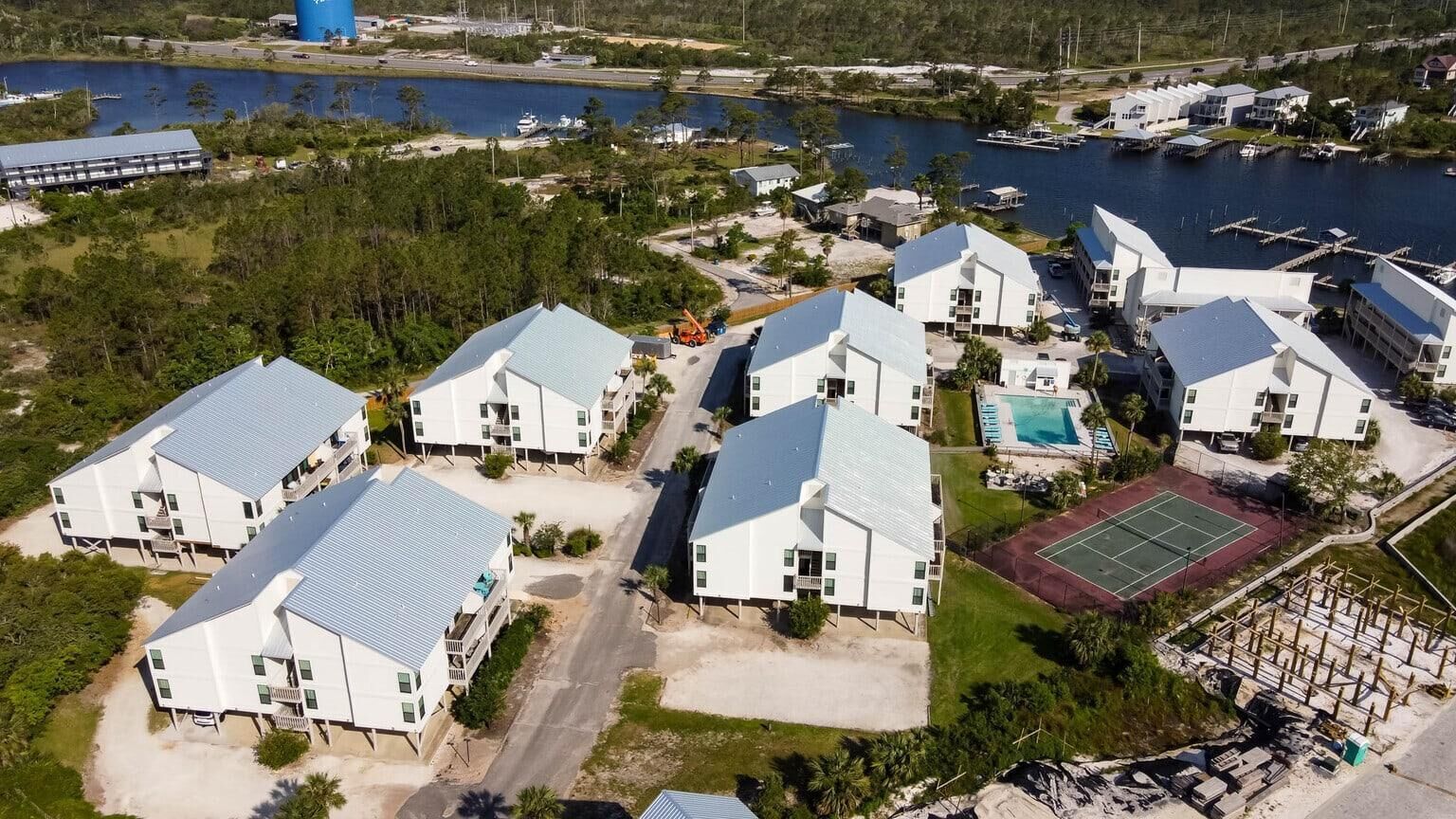 A coastal residential area with modern white buildings, a tennis court, and a swimming pool.