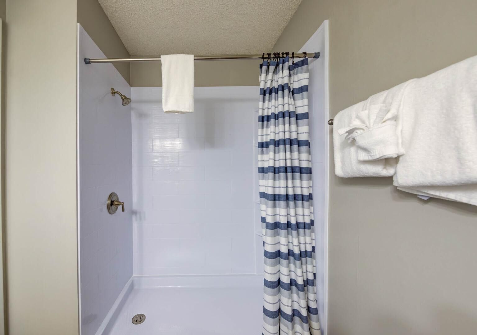 Une douche avec un rideau blanc et un porte-serviettes sur lequel est posée une serviette.