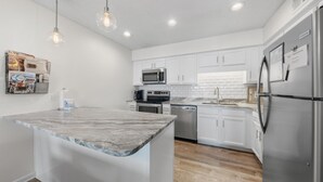A modern kitchen with white cabinets, stainless steel appliances, and a marble countertop island. - Cotton Bayou 7H (Orange Beach)