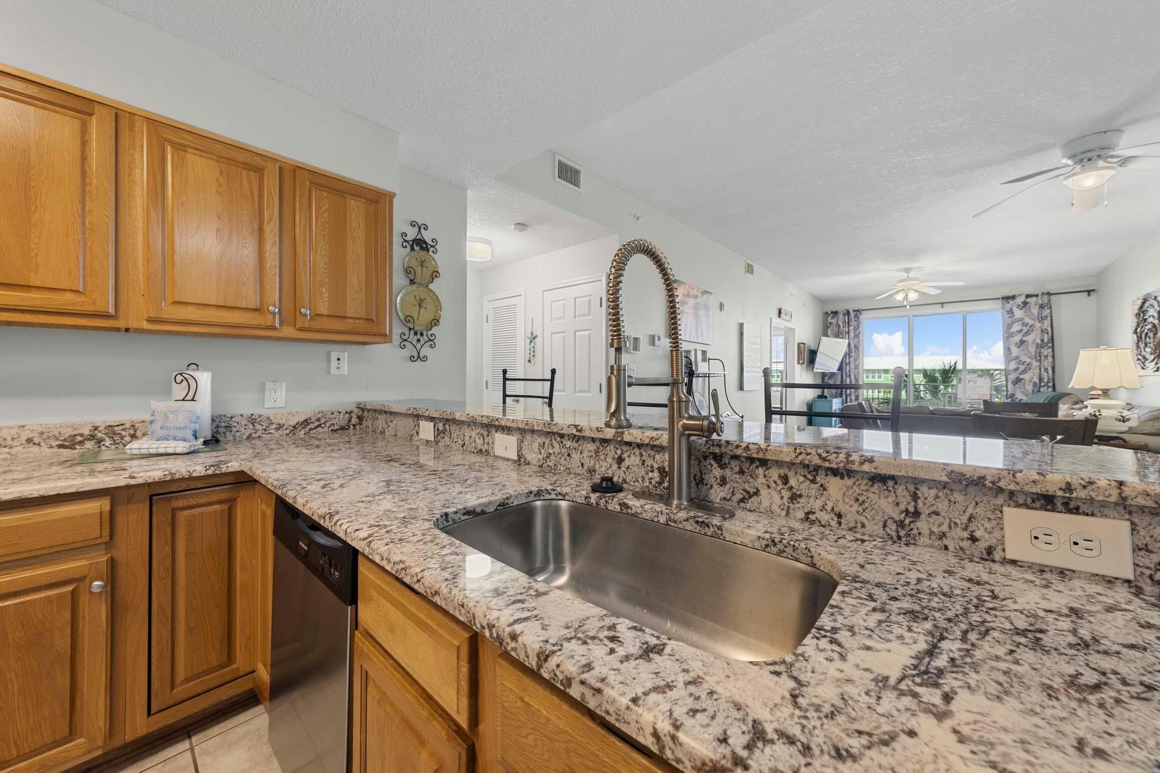A kitchen with granite countertops, wooden cabinets, a stainless steel sink, and a ceiling fan.