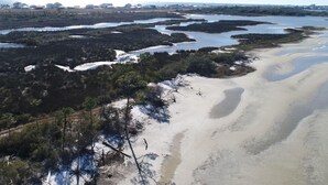 An aerial view of a coastal area with sandy beaches, patches of vegetation, and a distant shoreline.