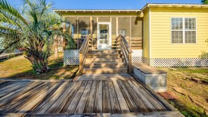 A wooden deck leading to a yellow building with a door and windows. - The Rookery 2202 (Gulf Shores)