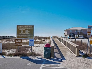 A beach access sign, a trash can, and a wooden boardwalk leading to a building. - The Rookery 2202 (Gulf Shores)