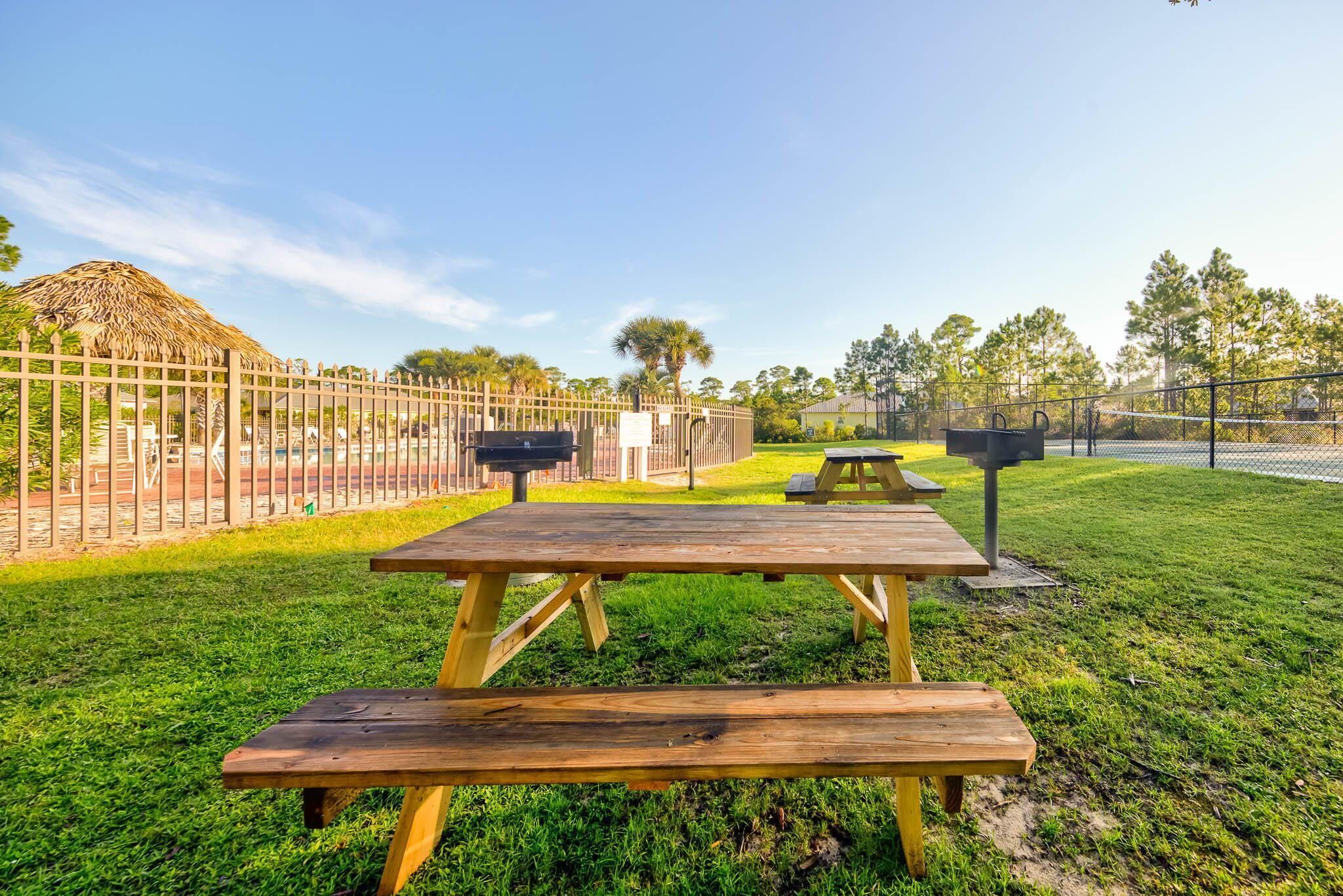 A picnic table with benches in a park area, surrounded by a fence and trees.