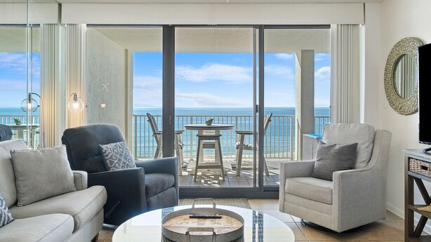 Un soggiorno moderno con un'ampia porta scorrevole in vetro che si apre su un balcone con vista sull'oceano. Nella stanza ci sono due divani e un tavolino da caffè.