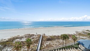 Vista sulla spiaggia con binari ferroviari, palme e cielo sereno.