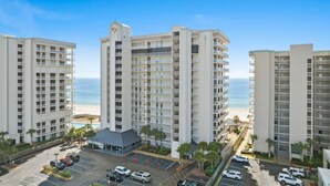 Un hotel di grandi dimensioni con numerosi piani, un parcheggio e vista sulla spiaggia.