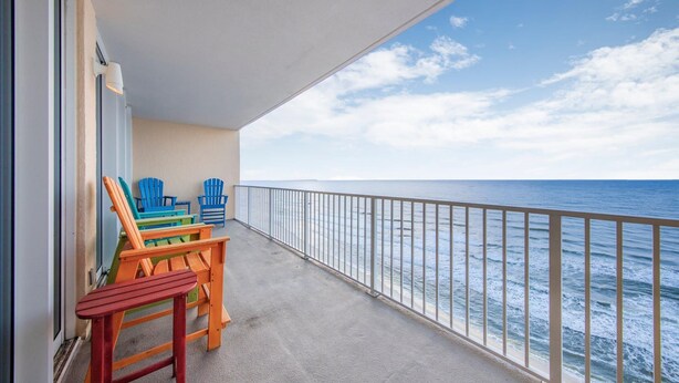 A balcony with a view of the ocean, featuring a railing and a few colorful chairs.