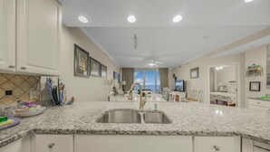 A modern kitchen with granite countertops, white cabinetry, and a stainless steel sink.