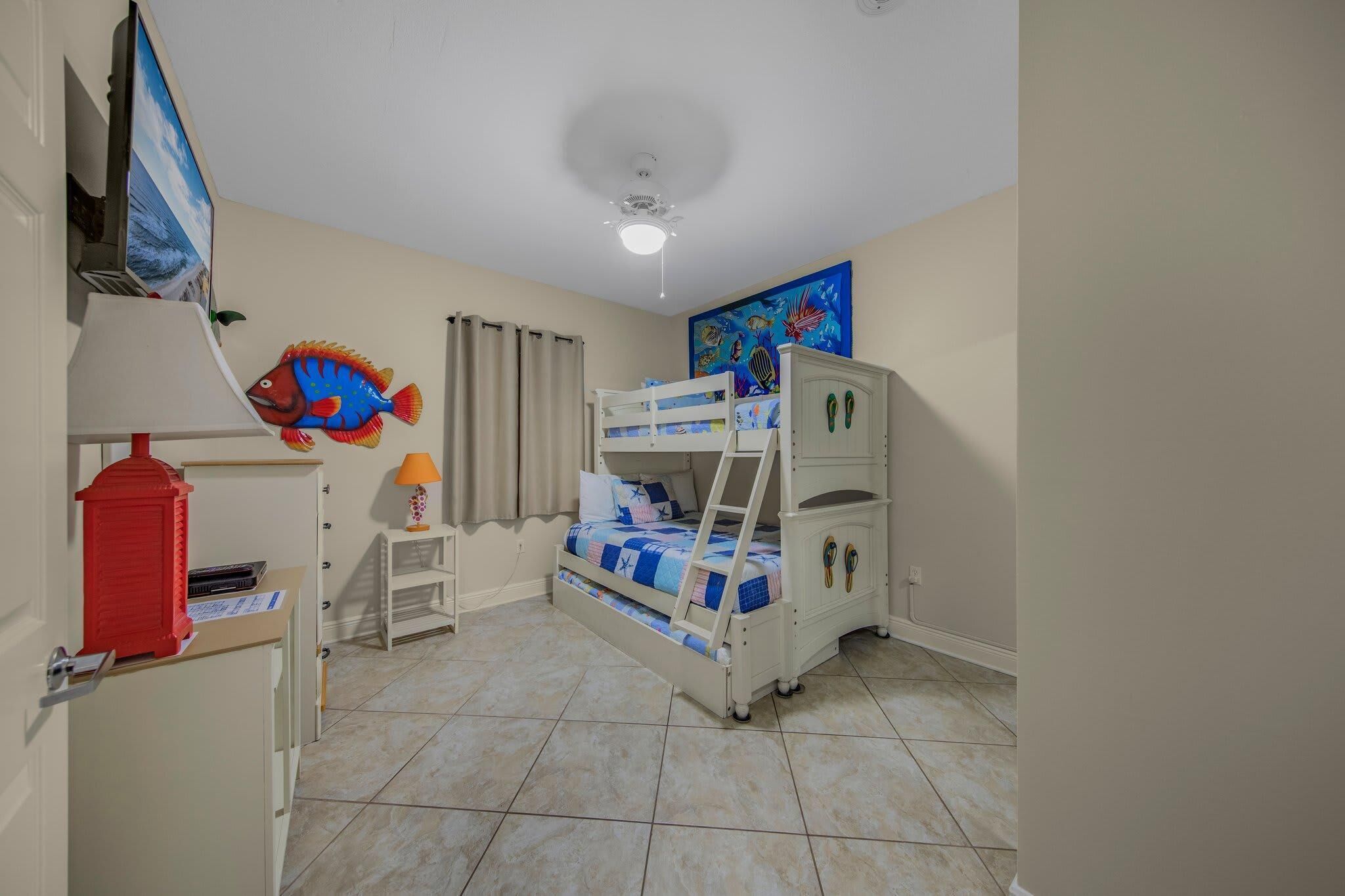 A child's bedroom with bunk beds, a desk, a lamp, and a fish wall decoration.