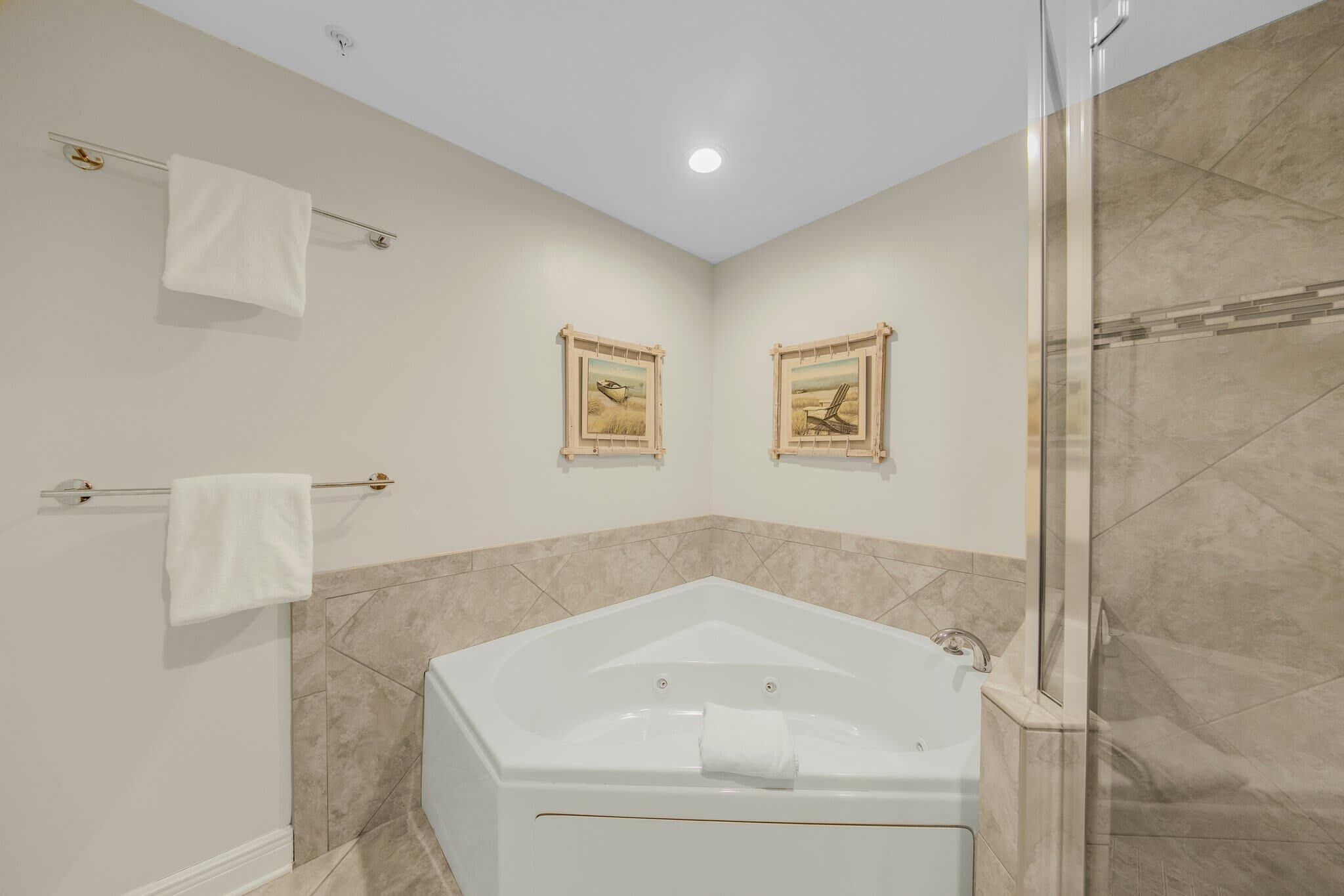 Un baño moderno con una bañera grande, dos cuadros enmarcados en la pared y un box de ducha de vidrio.