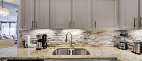 A modern kitchen with white cabinets, a granite countertop, a built-in dishwasher, and a stone backsplash.