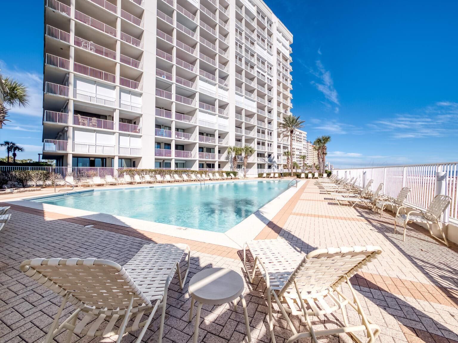 Un hotel con una piscina amplia, varios balcones y zonas de estar al aire libre.