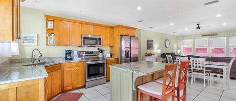 A kitchen with wooden cabinets, a granite countertop, stainless steel appliances, and a dining area with a bench and chairs.