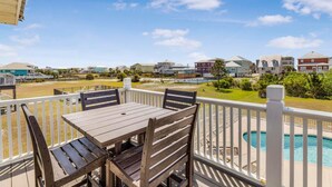 A balcony with a table and chairs, a pool, and a view of surrounding buildings. - Sandy Feet Retreat (Gulf Shores)