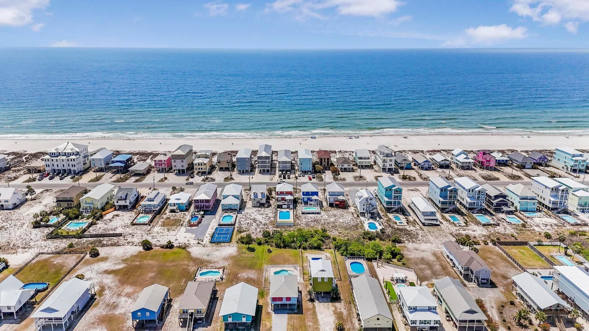 Vista aerea di una zona residenziale costiera con case, piscine e una spiaggia.