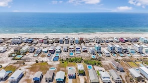 An aerial view of a coastal residential area with houses, swimming pools, and a beach.