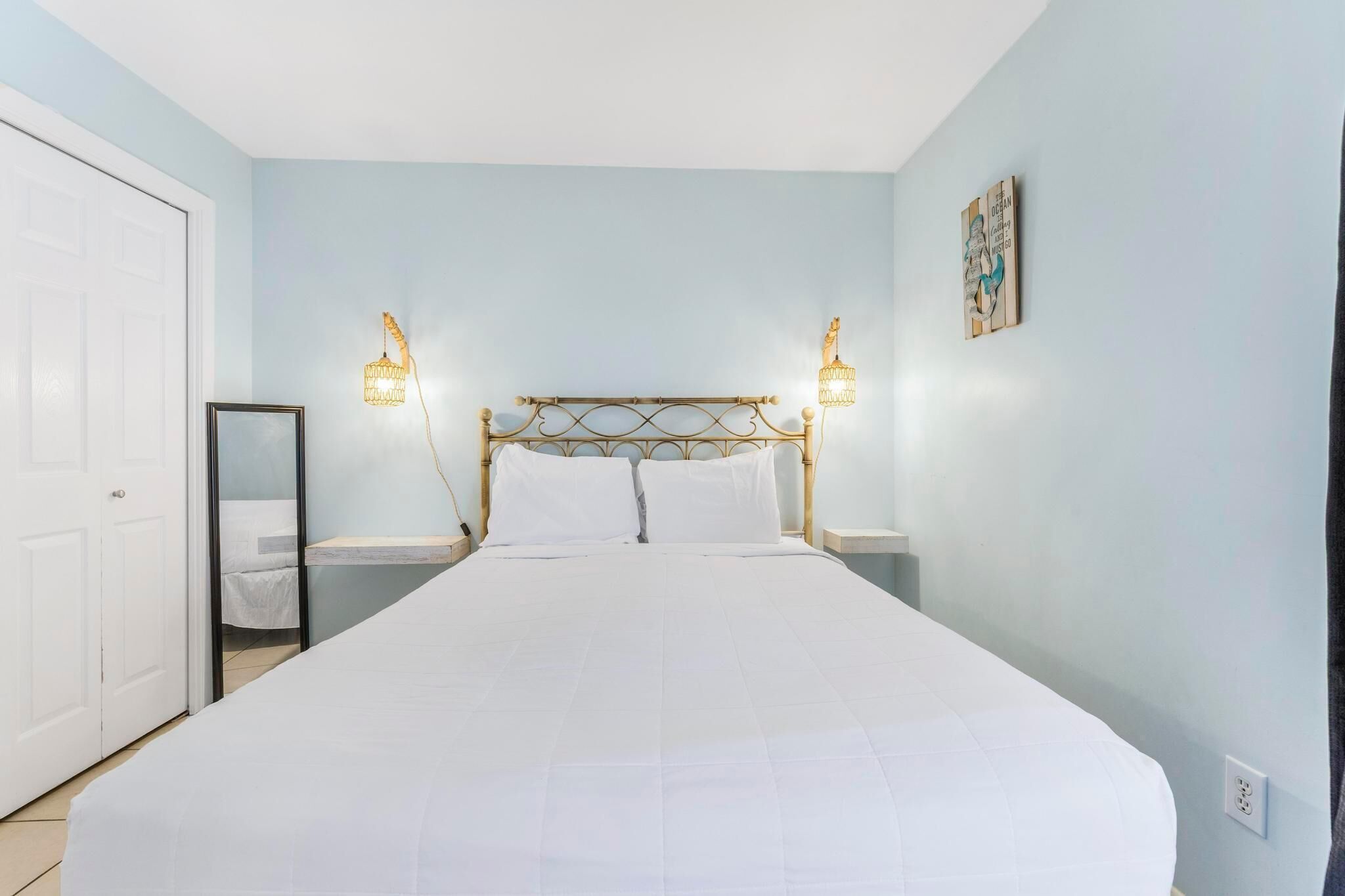 A bedroom with a bed, a bedside table, a nightstand, a mirror, and wall-mounted lights.