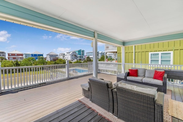 A covered deck with outdoor furniture, a pool, and a view of neighboring houses.