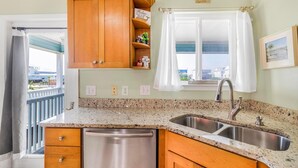 A kitchen with granite countertops, stainless steel sink, wooden cabinets, and a window with a view. - Sandy Feet Retreat (Gulf Shores)