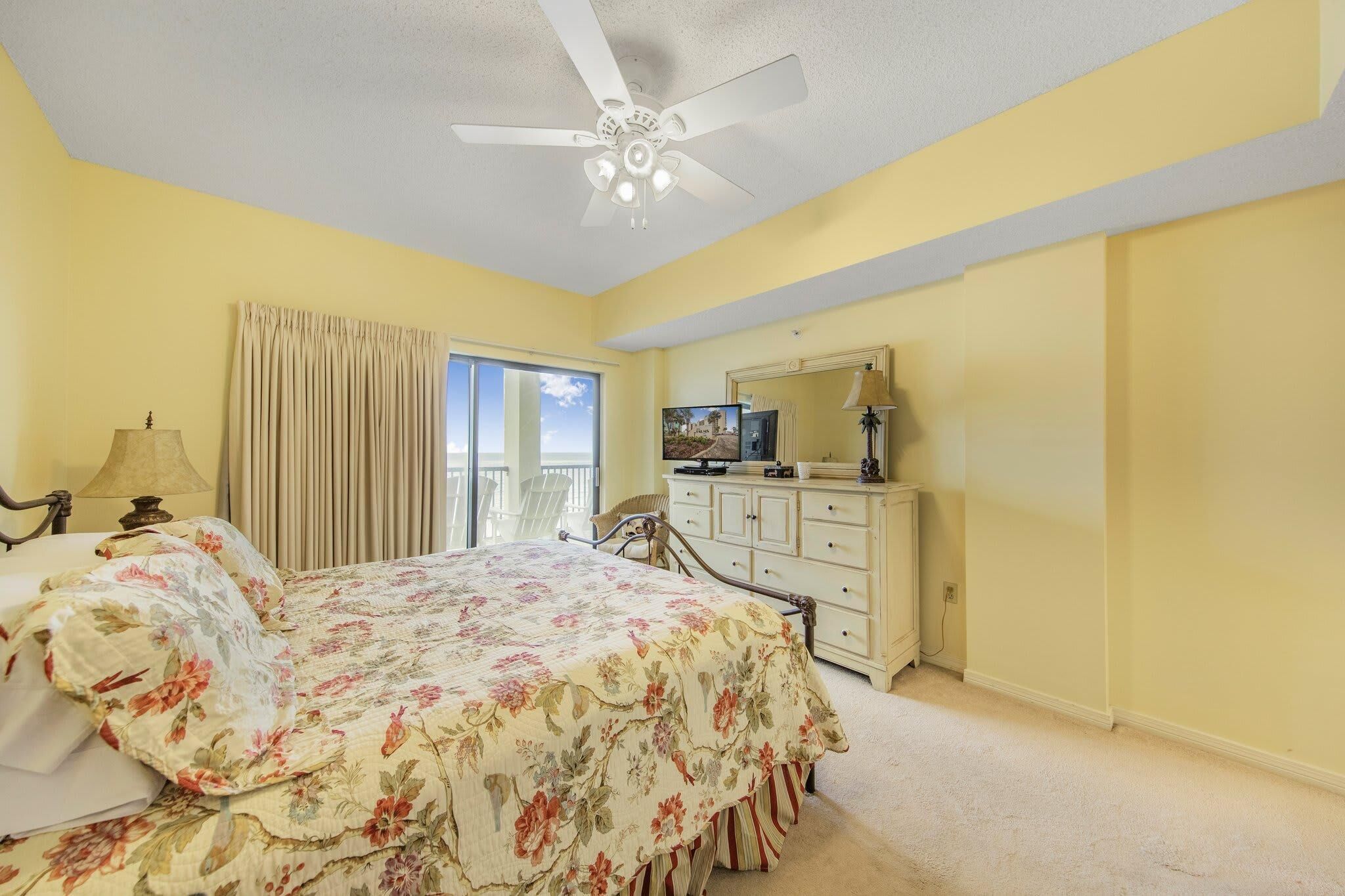 A bedroom with a bed, a dresser, a television, and a ceiling fan.