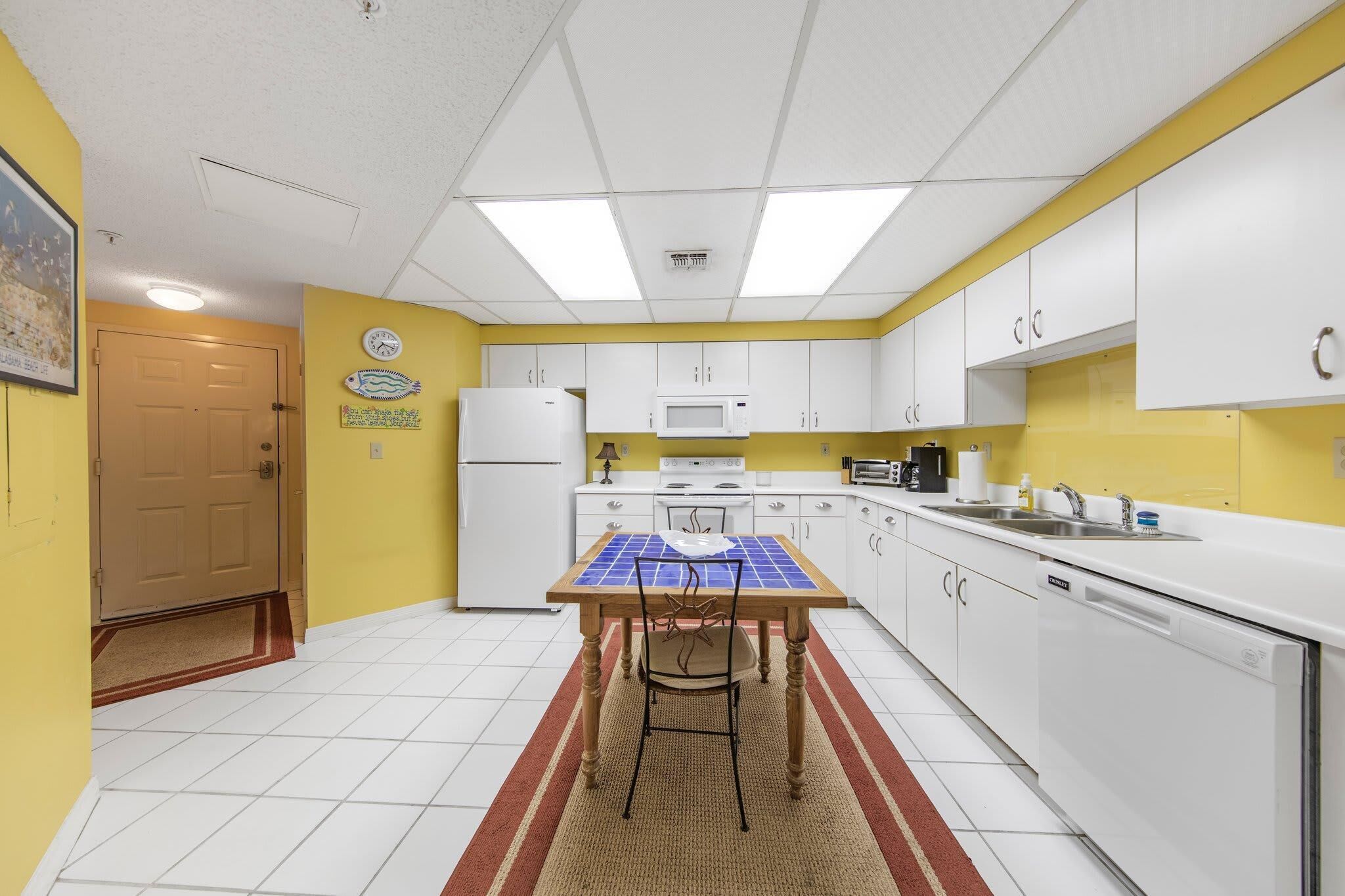Cocina compacta con armarios blancos, microondas, refrigerador y mesa con energía solar.