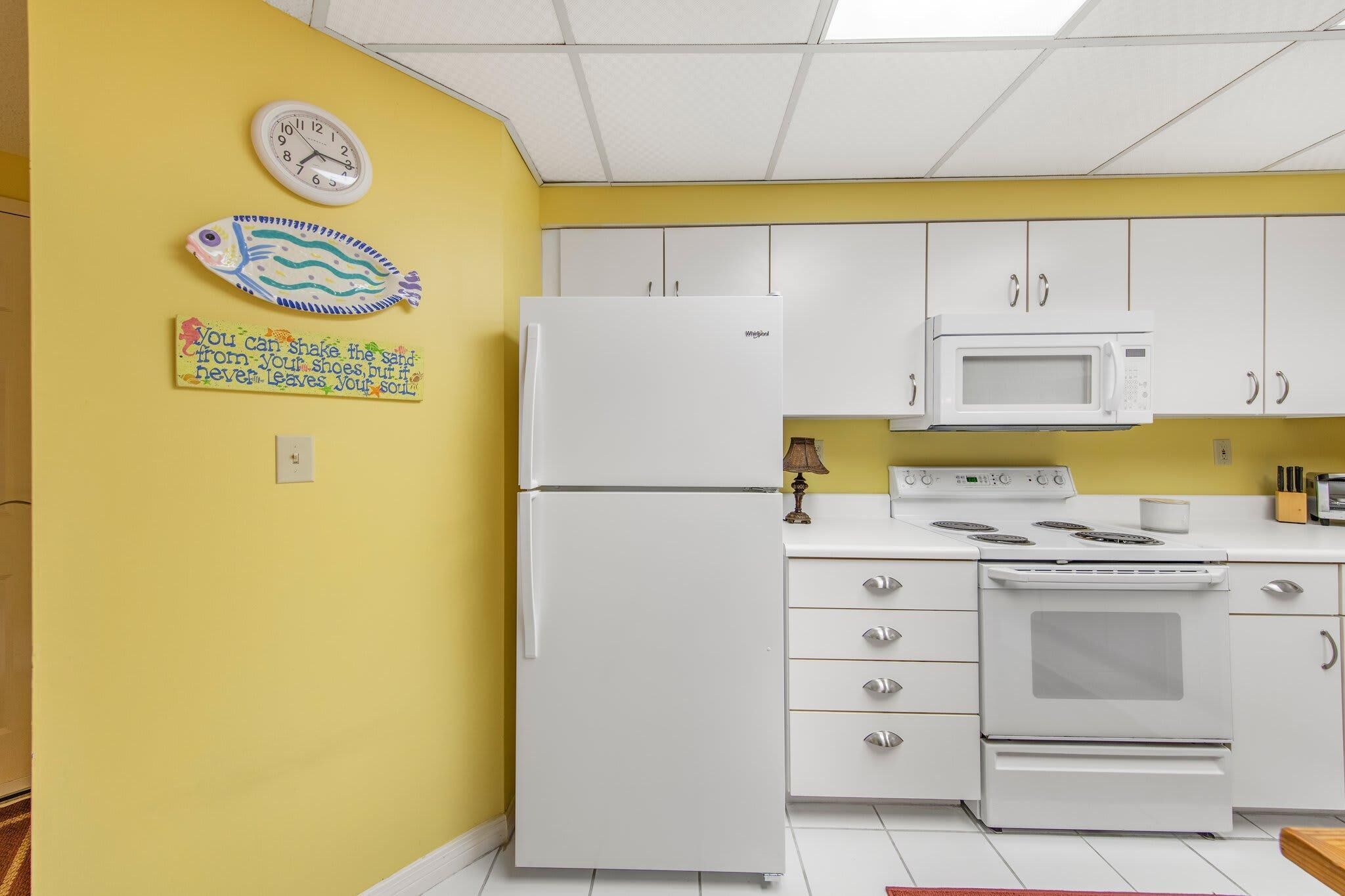 A kitchen with white appliances, yellow walls, and a clock on the wall.