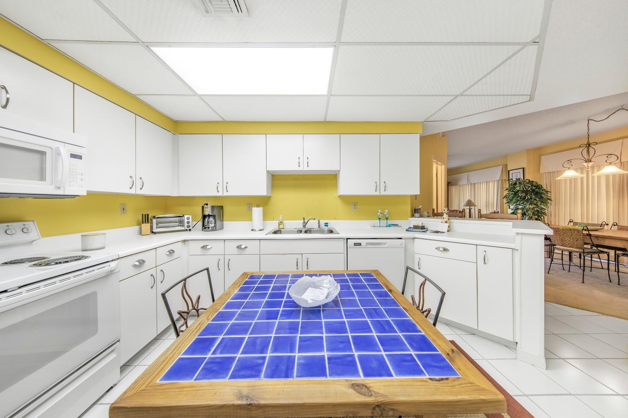 A modern kitchen with white cabinets, a yellow accent wall, and a blue-tiled island.
