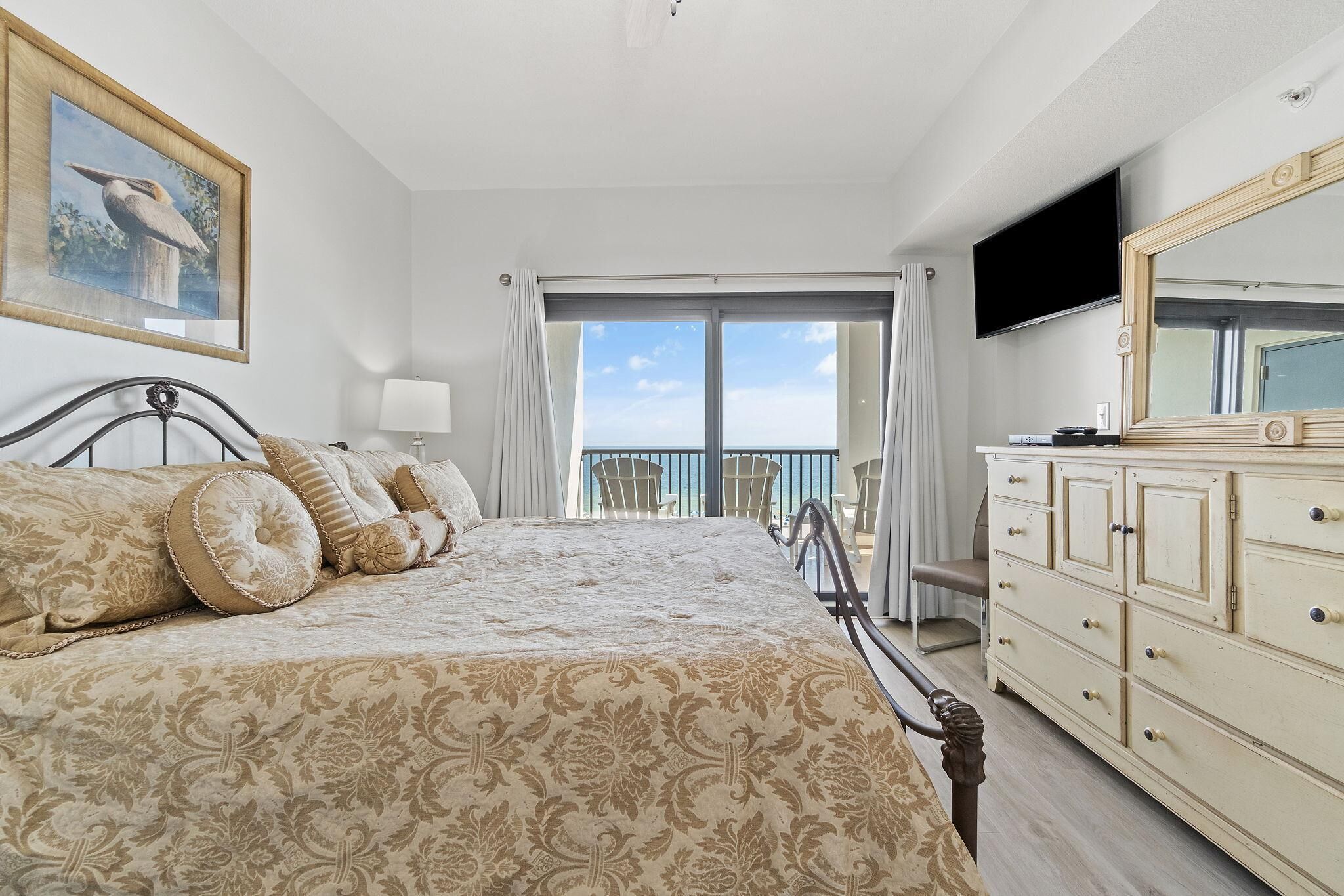 A bedroom with a large bed, a dresser, a television, and a balcony with a view.