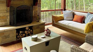 Ein gemütliches Blockhaus-Interieur mit Kamin aus Stein, Holzbalken, einer Hängeschaukel und einer Couch mit Kissen.