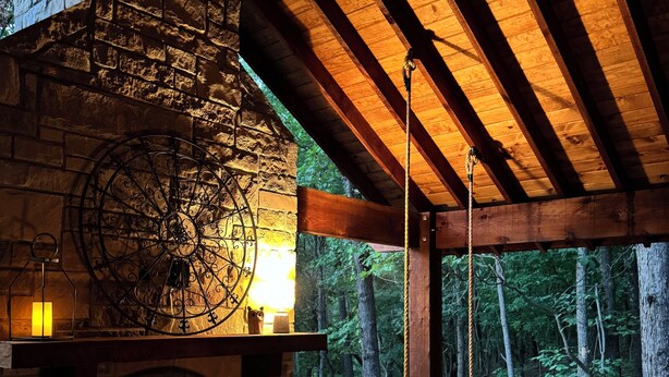 Ein gemütliches Blockhaus-Interieur mit Kamin aus Stein, Holzbalken, einer gepolsterten Sitzecke und Blick auf den Wald.