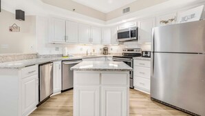 A modern kitchen with white cabinets, stainless steel appliances, and a granite countertop. - Summer House 1405a (Orange Beach)