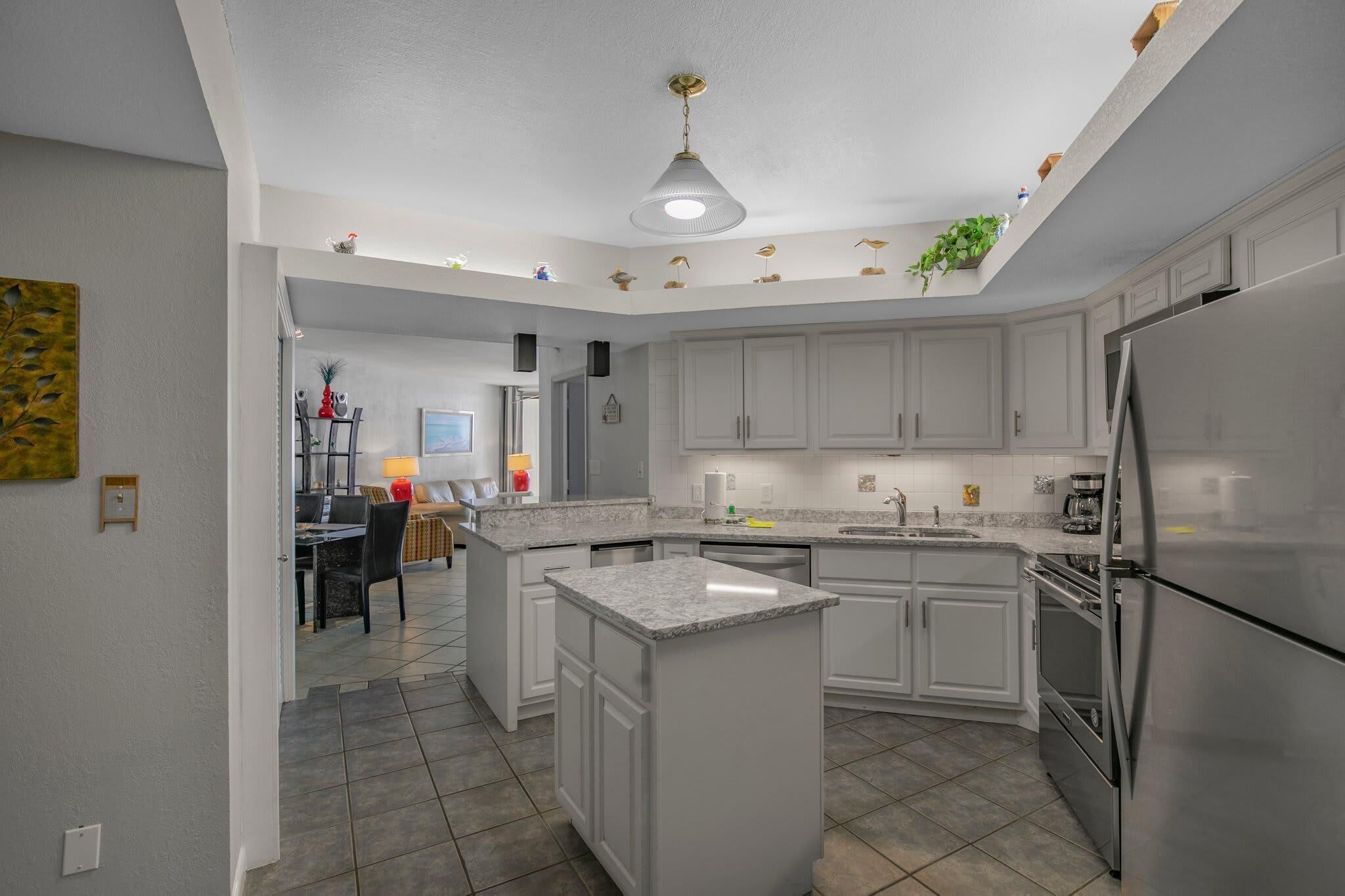 A modern kitchen with white cabinets, a central island, stainless steel appliances, and a ceiling light fixture.