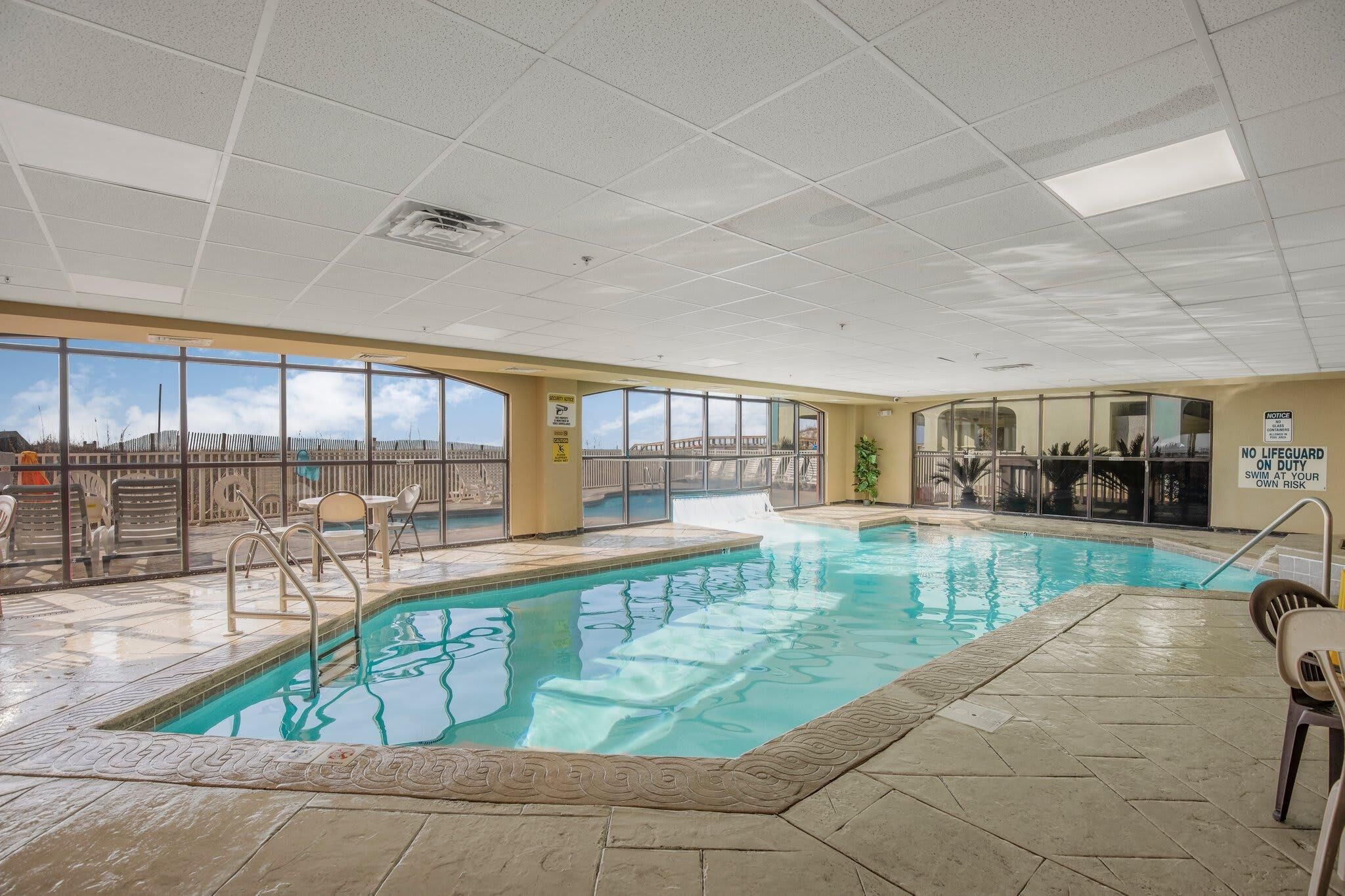 Una piscina interior con vistas despejadas a través de amplias ventanas, suelo de baldosas y un cartel de 'no hay socorrista'.